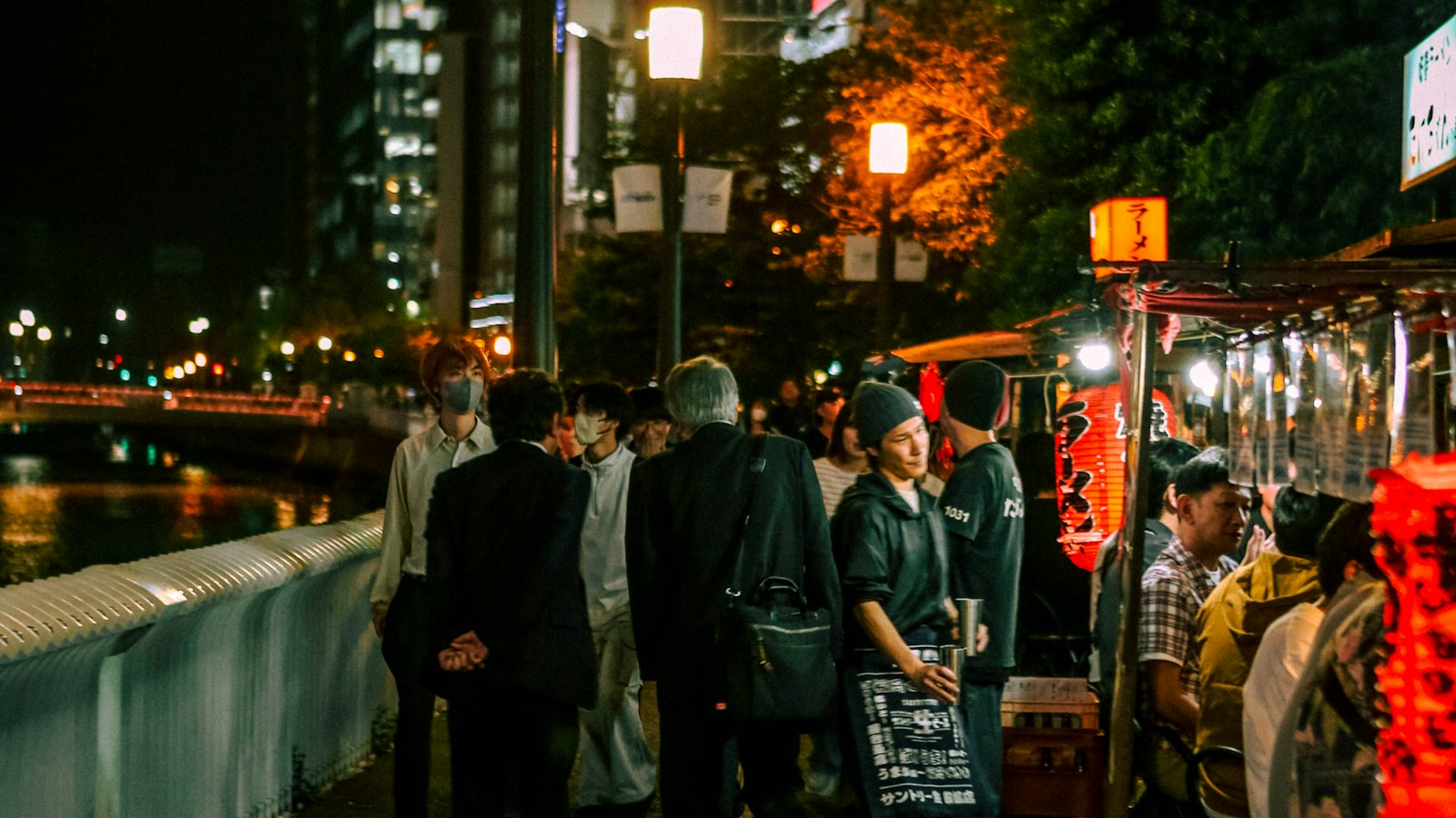 People gathered at open-air food stalls beside the water at night