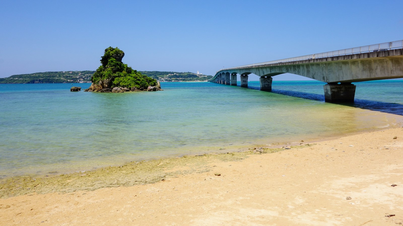 The Kouri Bridge crossing turquoise water beside a small rocky islet